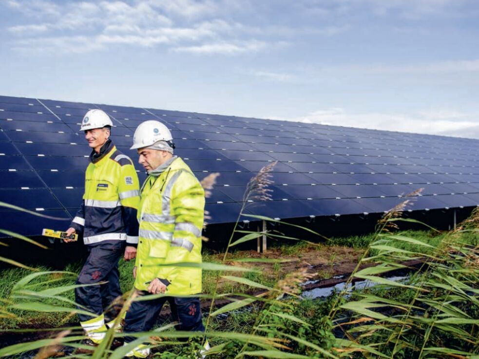 Zwei Menschen in Arbeitskleidung laufen an einem großen Solarpanel entlang.