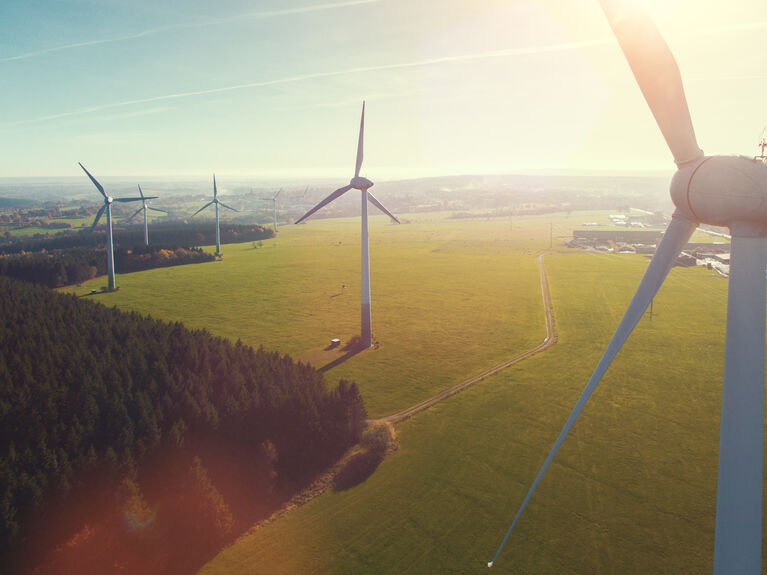 Windkraftanlagen stehen in einer grasbewachsenen Landschaft unter einem hellen, sonnigen Himmel.